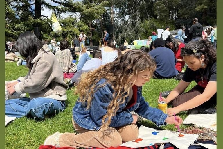 Attendees of an outdoor music and sustainability festival paint canvas tote bags
