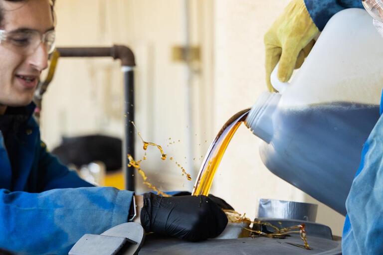 Photo of two members of BTC pouring biodiesel while wearing safety equipment