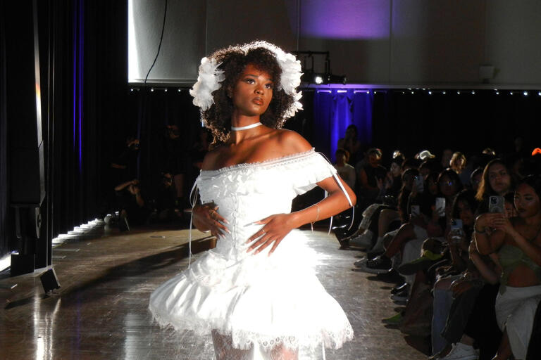 Photo of a student model on a runway posing in a white dress