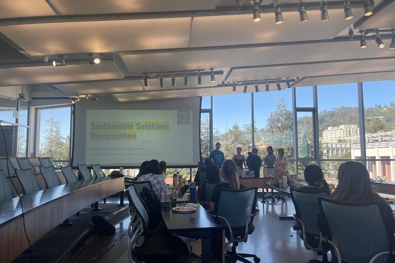 Photo of classroom with people sitting at desks and a group presenting a presentation at the front