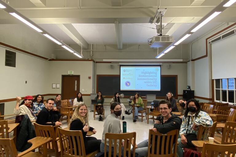 Group of students in a classroom smiling with a sign in the background that says "Highlighting Environmental Intersectionality within UC Berkeley"